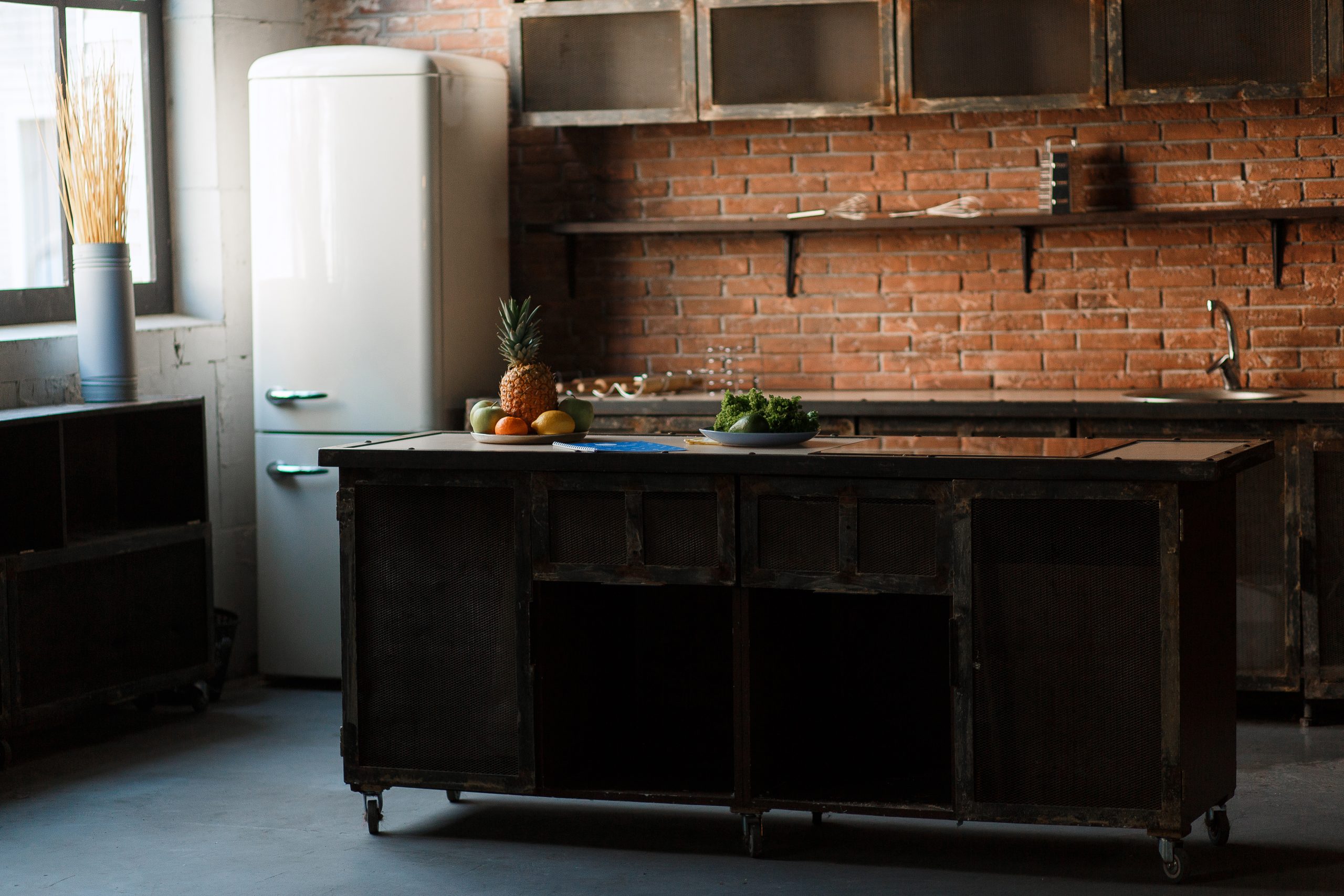 Dark loft kitchen with red brick wall. Kitchen table Cutlery, spoons, forks, breakfast fruit, fridge. Morning natural sunlight.