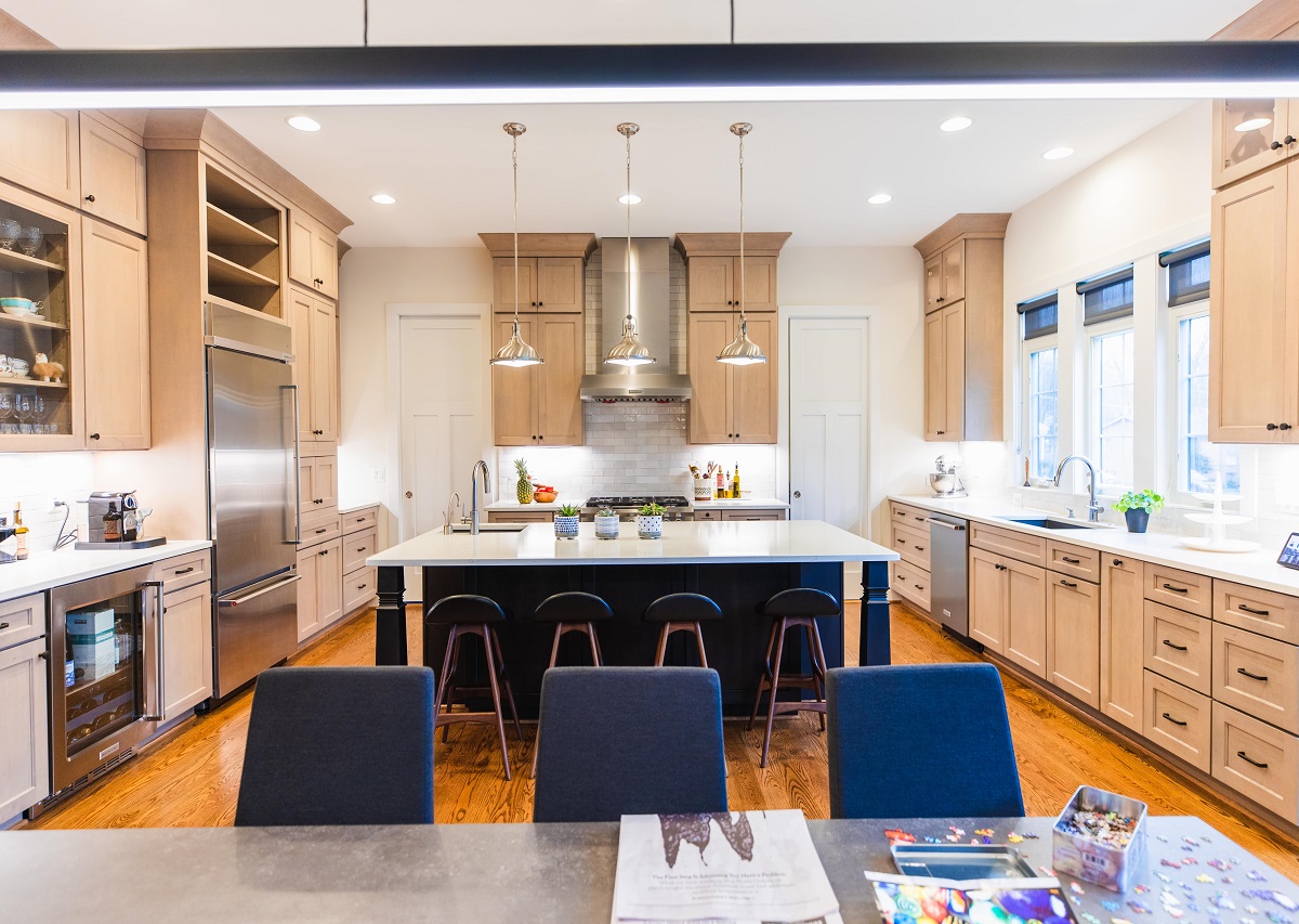 Spacious kitchen remodel with light wood cabinetry, a large central island with seating, stainless steel appliances, pendant lighting, and warm hardwood floors designed for both daily use and visual balance.