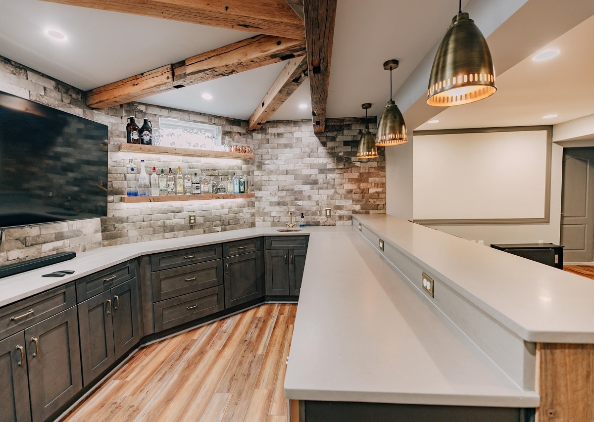 Basement remodeling in Northern Virginia with a custom wet bar, stone accent wall, wood beam ceiling details, and built-in cabinetry creating a functional entertainment area that adds livable space in the DC area.