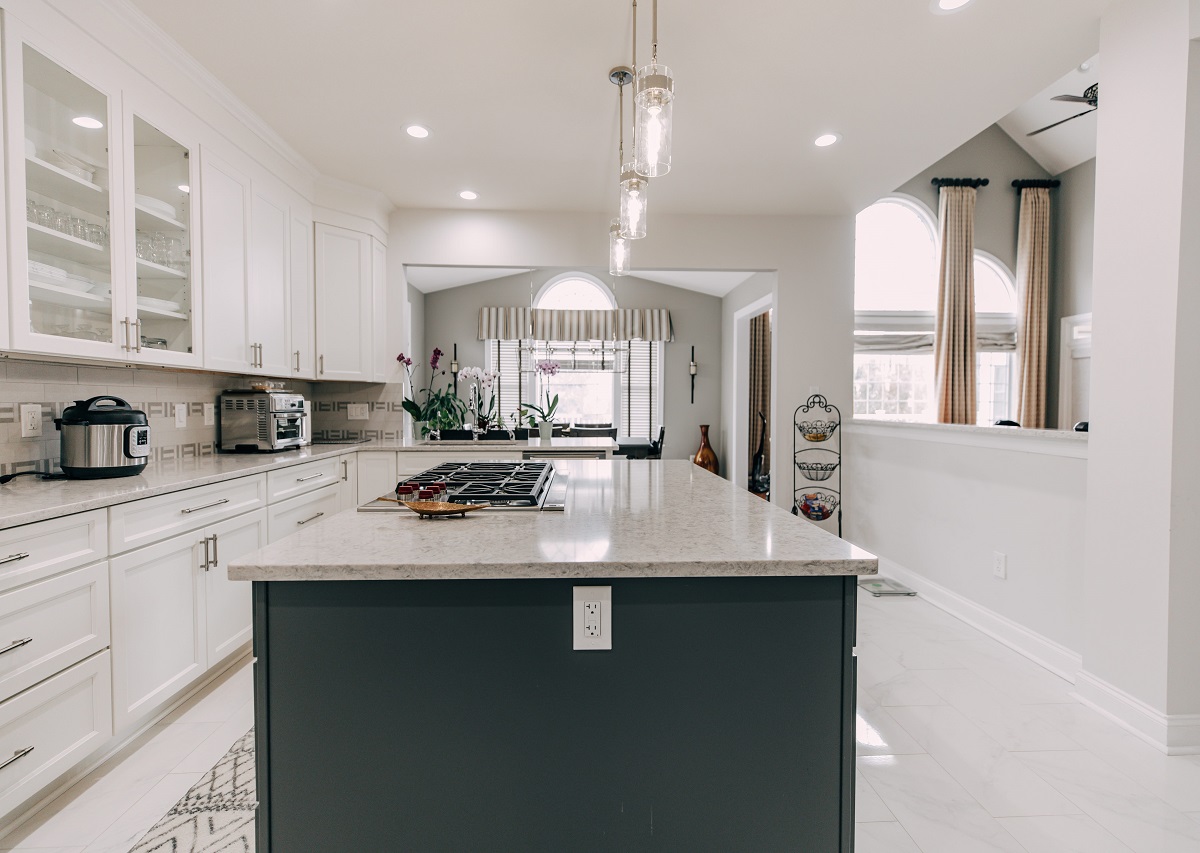 Spacious kitchen with a light speckled granite island countertop, white cabinets, glass pendant lights, and open layout design