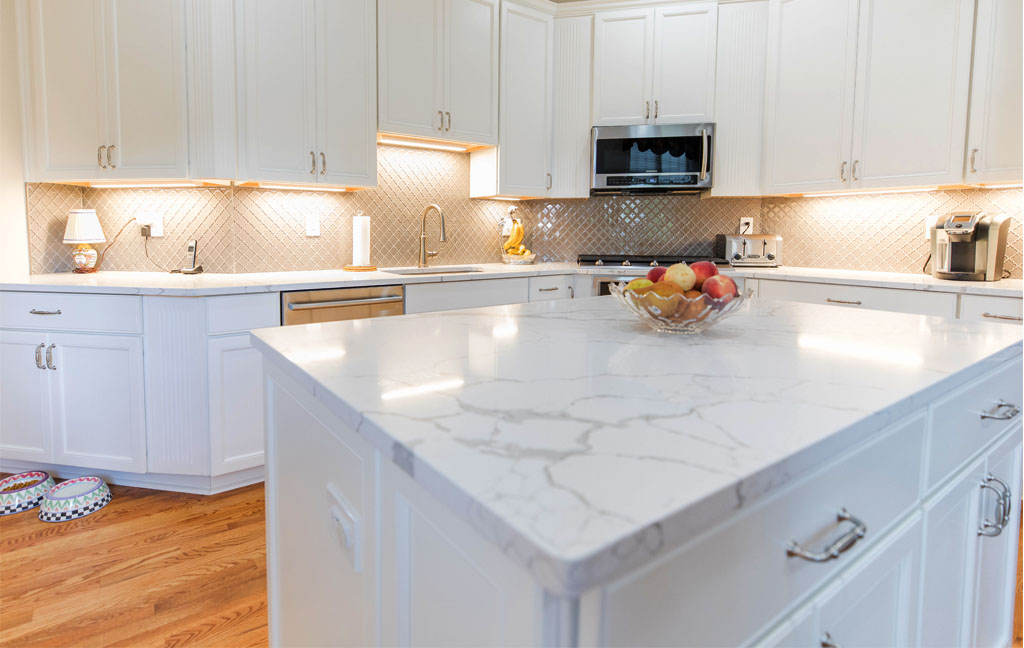 White quartz kitchen island countertop with subtle gray veining in a modern kitchen remodel with white cabinets and warm lighting
