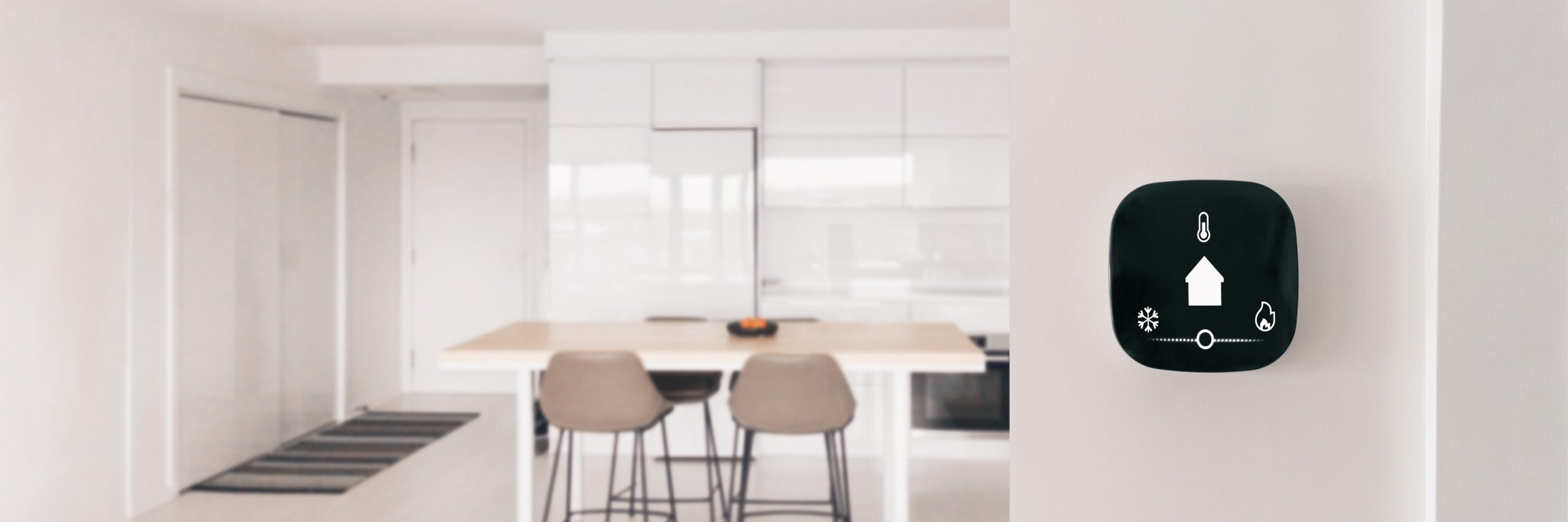 Smart home thermostat mounted on a wall near a modern kitchen, showing temperature control features for connected home comfort and efficiency.