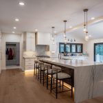 open concept kitchen remodel with marble waterfall island, white cabinets, bar seating, and pendant lighting