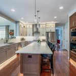 Two-tone kitchen renovation with gray upper cabinets walnut lower island quartz countertops and LED toe kick lighting