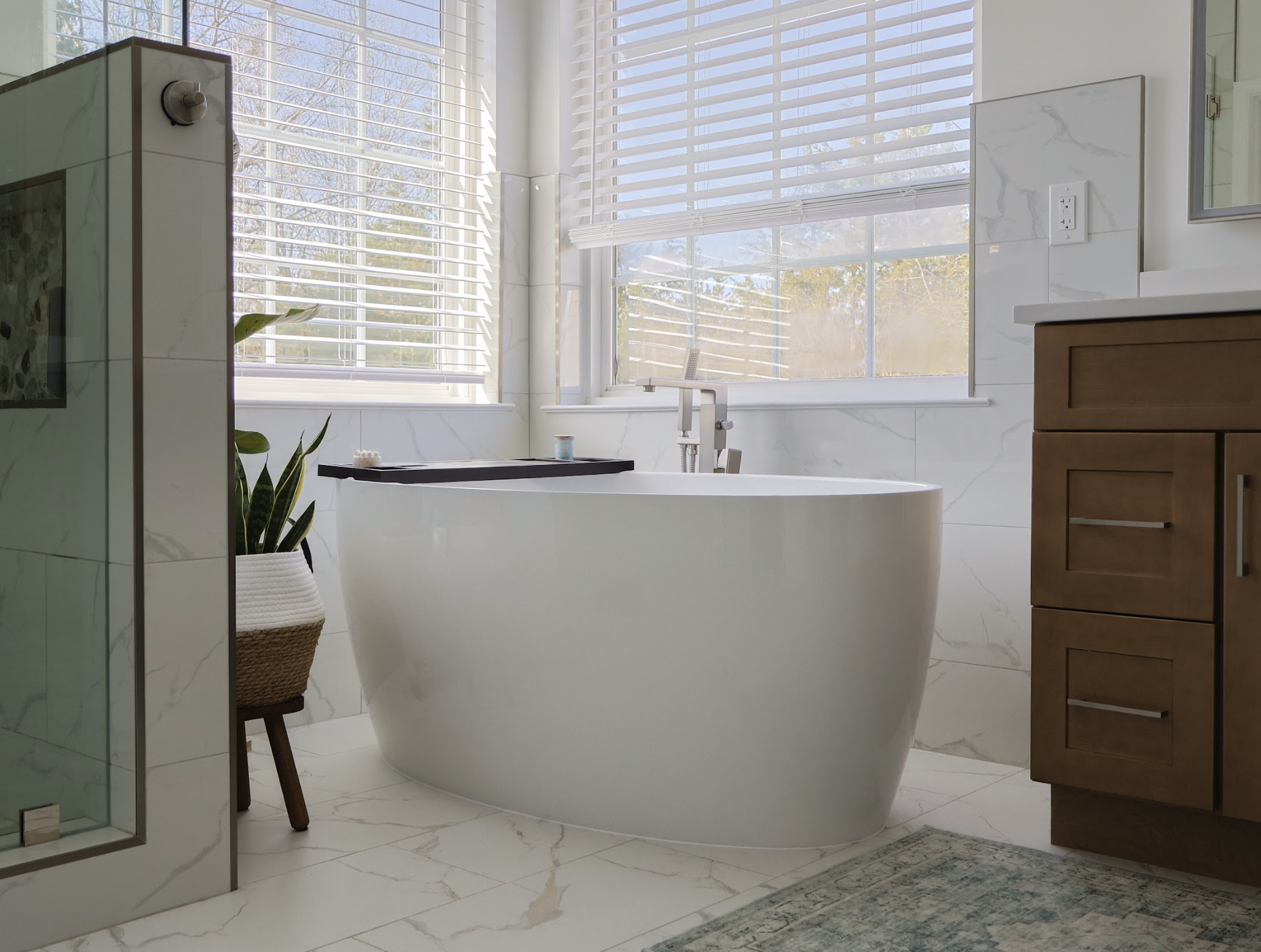 Bathroom remodel with a freestanding oval soaking tub, marble tile walls, and a glass walk-in shower nearby.