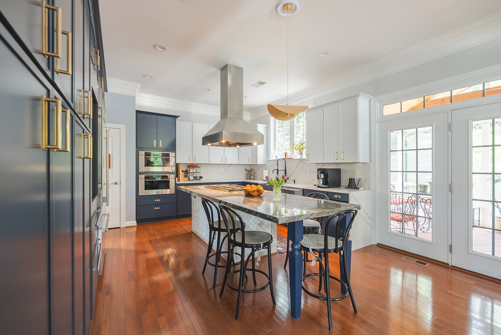 Kitchen renovation in Leesburg, VA with navy blue cabinets, brass hardware, a marble-look island, and a stainless range hood.